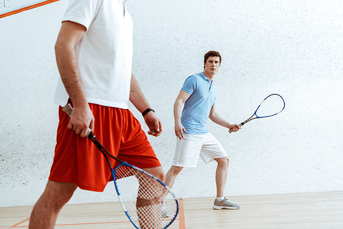 Cropped view of squash players with rackets in four-walled court
