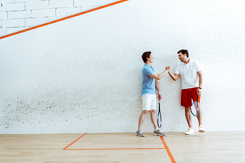 Full length view of squash players shaking hands in four-walled court