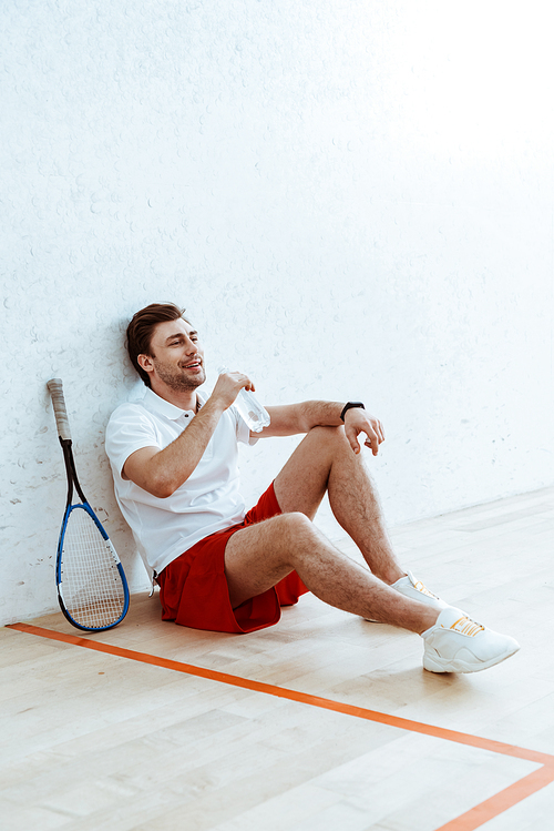 Squash player in red shorts sitting on floor and drinking water
