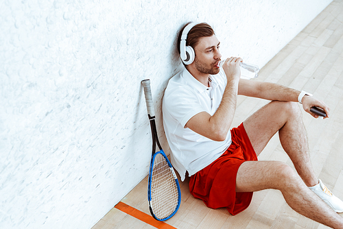 High angle view of squash player listening music in headphones and drinking water