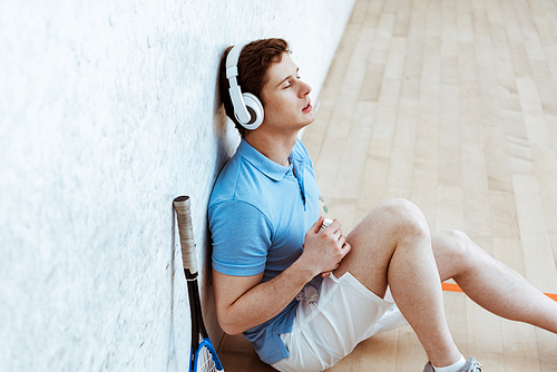 Squash player sitting on floor and listening music with closed eyes