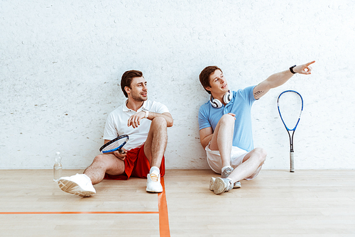 Squash player sitting on floor with friend and pointing with finger