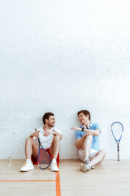 Smiling squash players sitting on floor and talking in four-walled court