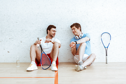Squash player sitting on floor and showing smartwatch to friend
