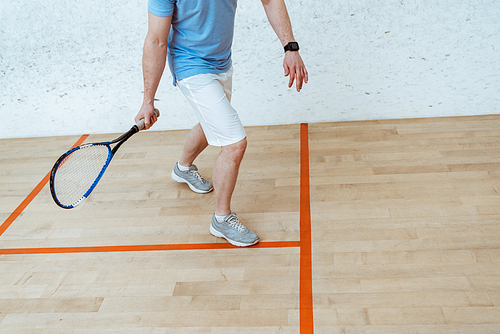 Partial view of sportsman with racket playing squash in four-walled court
