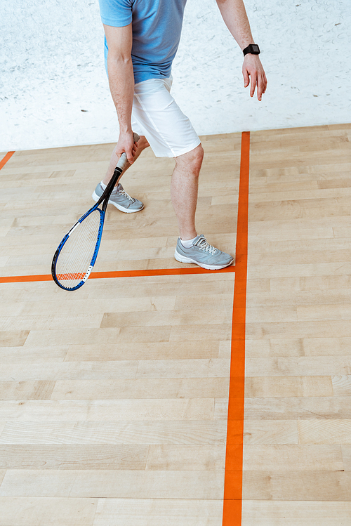 Partial view of sportsman with racket playing squash in four-walled court