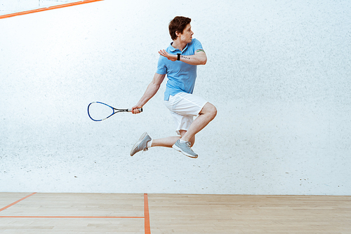 Sportsman in polo shirt jumping while playing squash in four-walled court