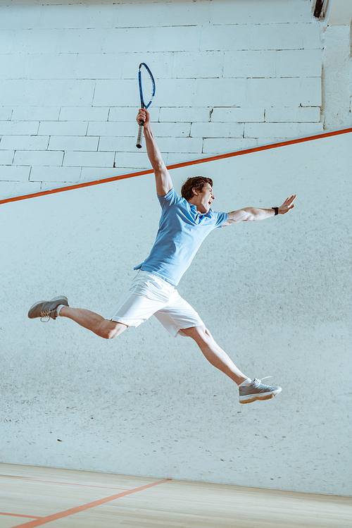 Full length view of excited sportsman in blue polo shirt jumping while playing squash