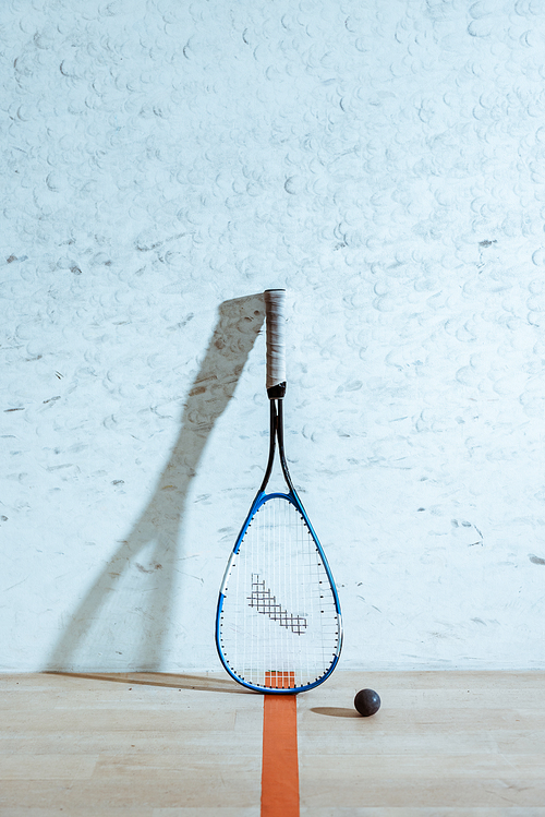 One squash racket and ball on wooden floor in four-walled court