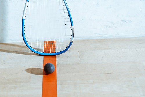 Squash racket and ball on wooden floor in four-walled court