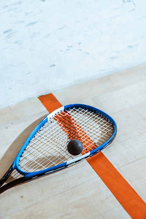 One squash racket and ball on wooden surface