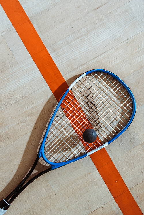 Top view of squash racket and ball on wooden surface