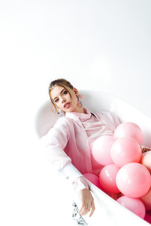 attractive young woman lying in bathtub with pink air balloons on white