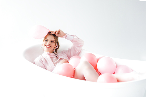 happy young woman lying in bathtub and holding pink air balloon on white