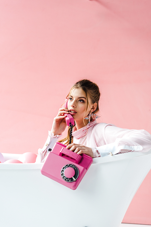 pretty girl talking on retro phone while lying in bathtub on pink