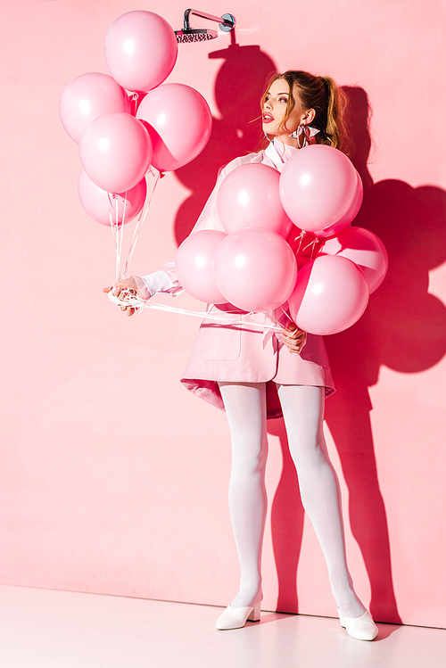 attractive young woman holding air balloons while standing on pink