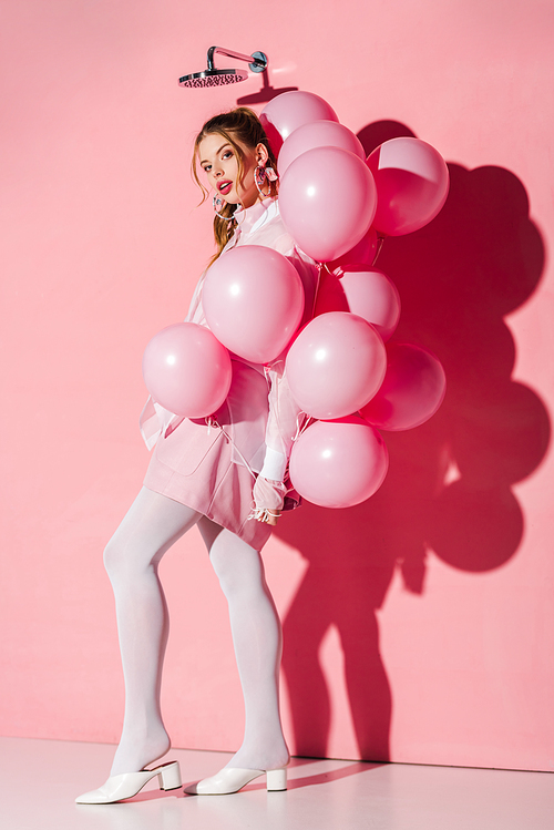 beautiful young woman holding air balloons while standing on pink