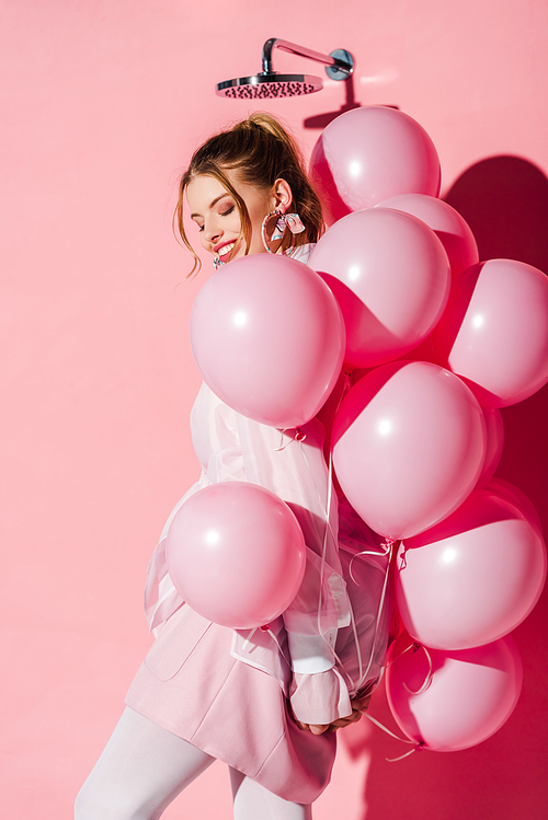 happy beautiful young woman holding air balloons while standing on pink