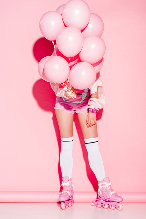 woman covering face with air balloons while standing in roller-skates on pink