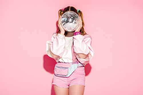 girl covering face with shiny disco ball while standing on pink