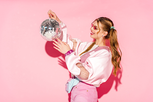 cheerful young woman looking at disco ball on pink