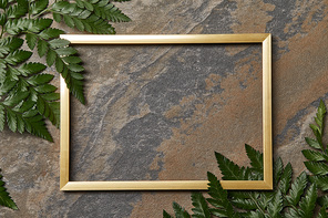 top view of empty golden frame on stone background with copy space and fern leaves