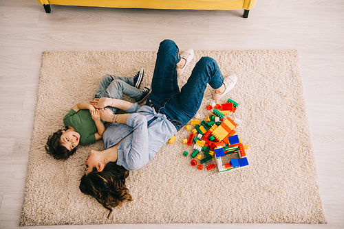 overhead view of smiling mom and son lying on carpet with toy blocks