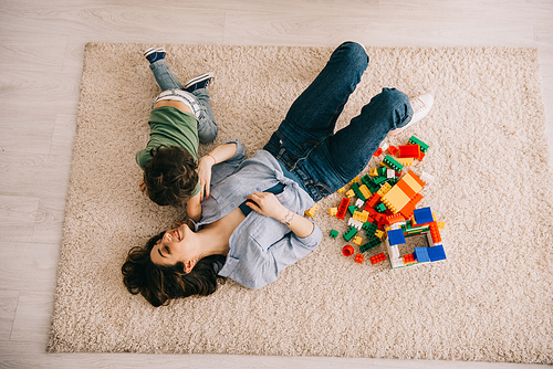 overhead view of smiling mom and son lying on carpet with toy blocks