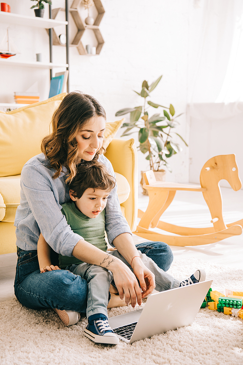 Mom and son sitting on carpet and using laptop