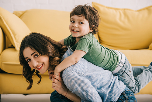 Smiling mother and son playing together near yellow sofa