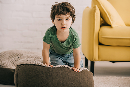 Front view of little boy in green t-shirt sitting on pouf