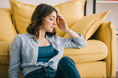 Tired woman sitting near yellow sofa with closed eyes