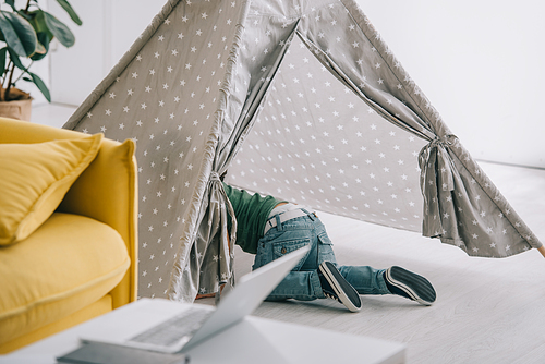 little boy in jeans playing in grey wigwam in living room