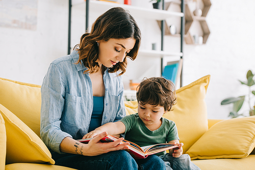 Mom and son sitting on yellow sofa and reading book