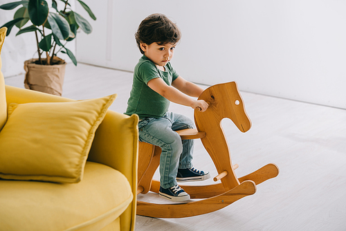 Cute little boy sitting on wooden rocking horse in living room