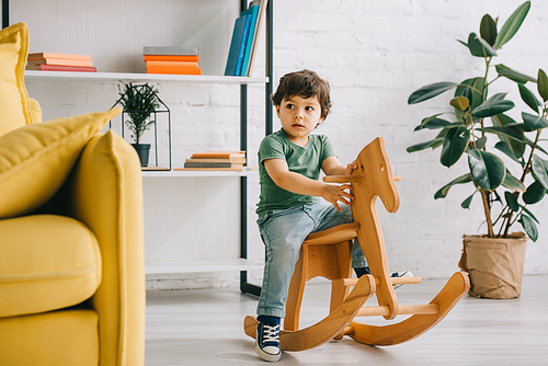 Cute child sitting on wooden rocking horse in living room