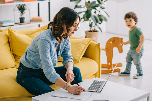 kid looking how mother working with laptop in living room