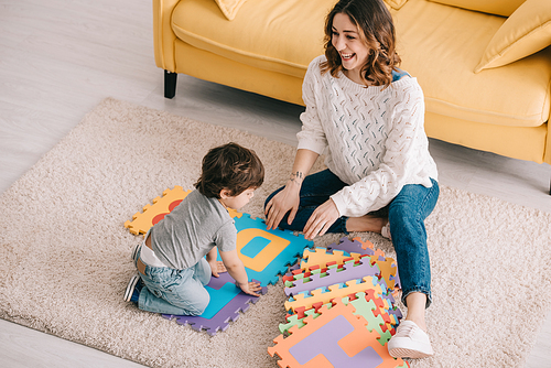 Mother and son playing with alphabet puzzle mat on carpet