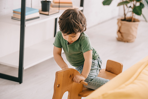 kid in green t-shirt playing with wooden rocking horse