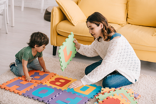 Mother and son playing with alphabet puzzle mat on carpet