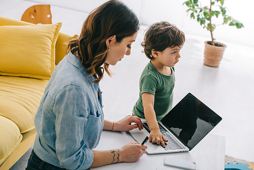 kid touching laptop while mother working in living room