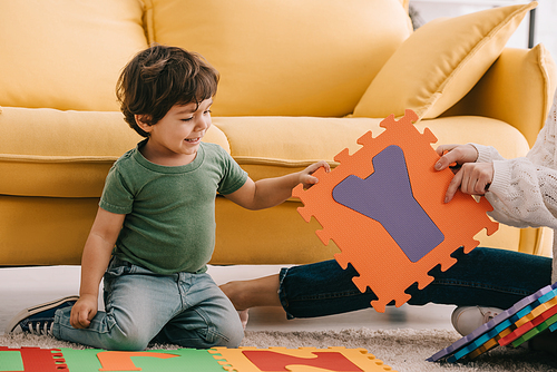 cropped view of mother and son playing with alphabet puzzle mat on carpet