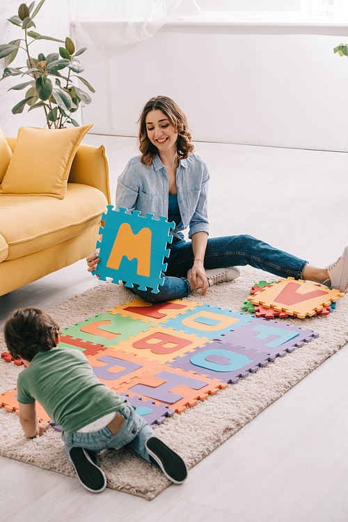 Smiling mother and kid playing with alphabet puzzle mat