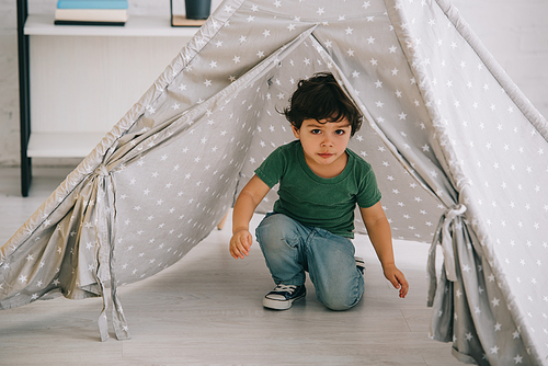cute kid in jeans sitting in grey wigwam at home