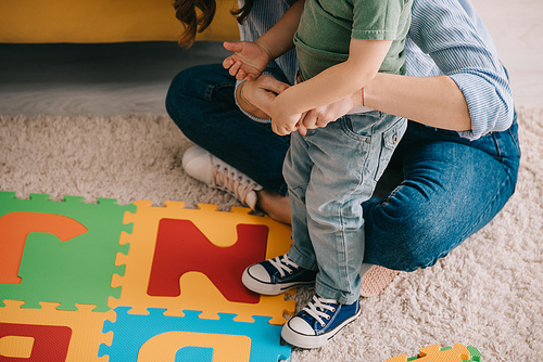 partial view of mother and son with alphabet puzzle mat on carpet