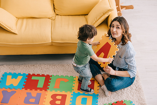 Smiling mother and kid playing with alphabet puzzle mat
