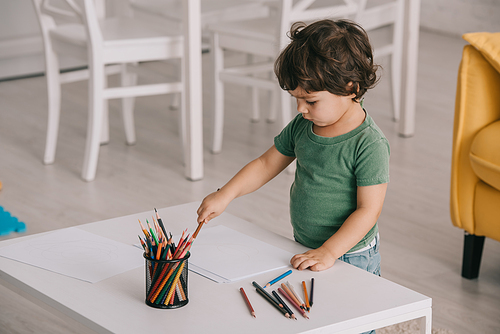kid in green t-shirt with color pencils and papers in living room