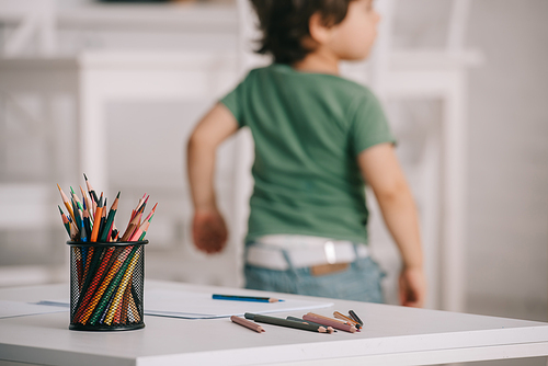 Selective focus of child near table with color pencils