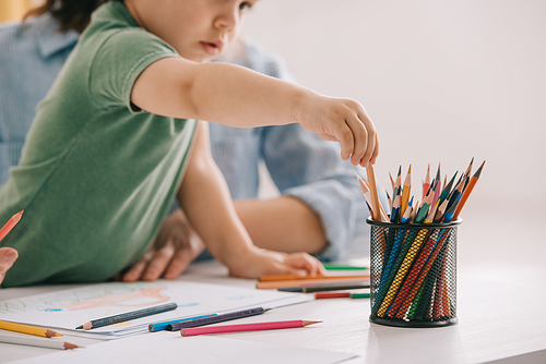 cropped view of mother and son drawing with color pencils in living room