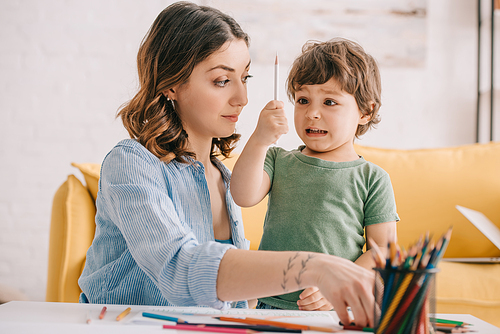 amazed kid holding color pencil while drawing with mom